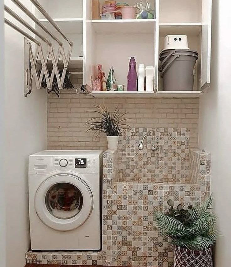 Compact service balcony utility area featuring a front-load washing machine, a decorative tiled built-in wash basin, white wall-mounted upper storage cabinets, and an accordion-style folding clothes drying rack.