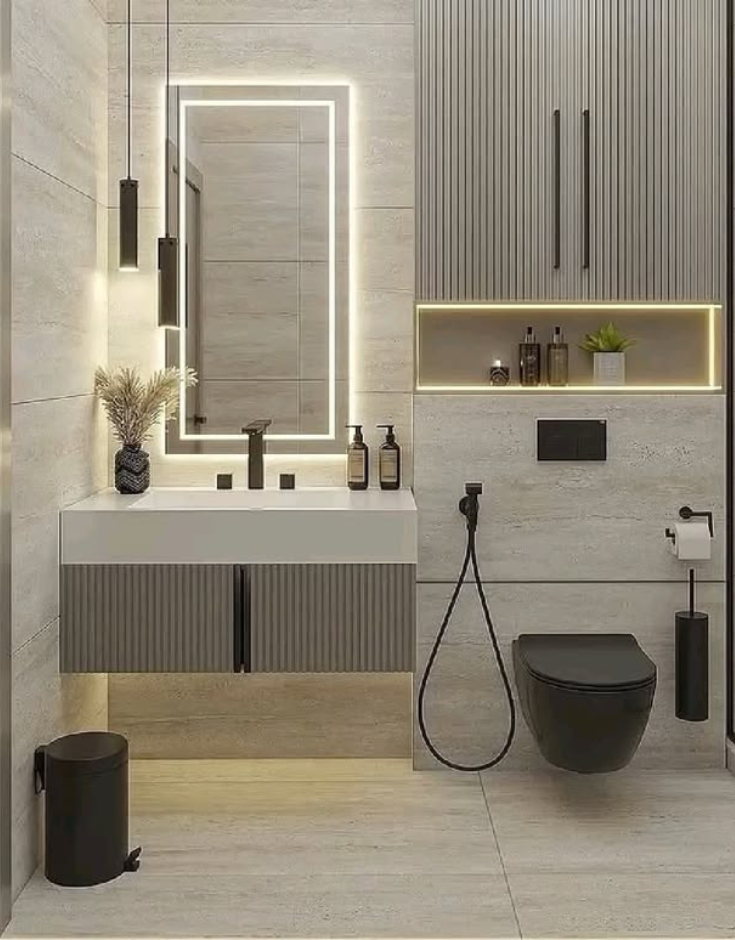 Modern compact bathroom interior showcasing a floating ribbed vanity unit, a matte black wall-hung toilet, a rectangular backlit mirror, modern black pendant lights, and a built-in wall niche with warm LED lighting.