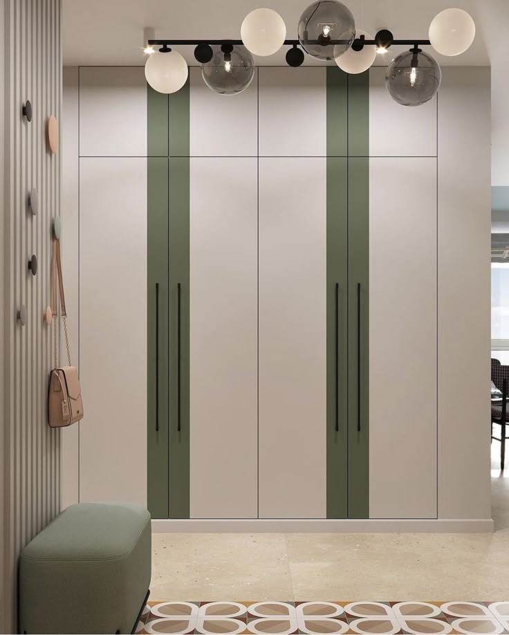 Modern floor-to-ceiling hinged wardrobe featuring off-white shutters with sage green vertical accent panels, extra-long matte black profile handles, seamless top loft storage, and a fluted wall panel with coat hooks.