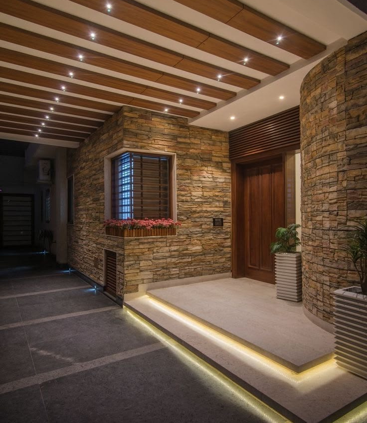 Luxury villa main entrance featuring rustic stacked stone exterior walls, a grand wooden front door, illuminated floating stone steps with warm LED strip lighting, and a slatted wood ceiling porch.