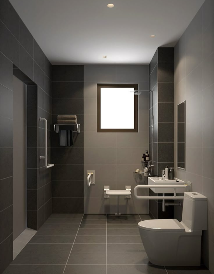 Modern accessible bathroom featuring matte grey anti-skid tiles, a wall-mounted shower seat, multiple white grab bars near the toilet and shower, a roll-under sink, and a curbless shower entry.