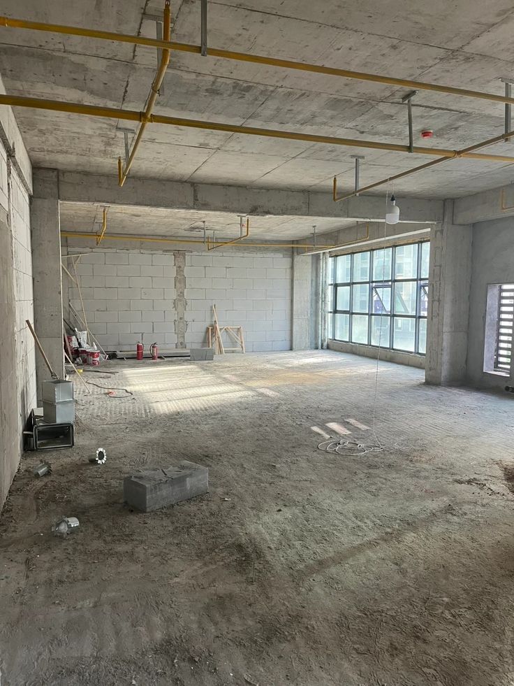 Houseway commercial shell interior fit-out and office construction services in Hyderabad, featuring a bare commercial workspace with exposed concrete ceilings, yellow fire sprinkler piping, cinder block walls, and large windows.